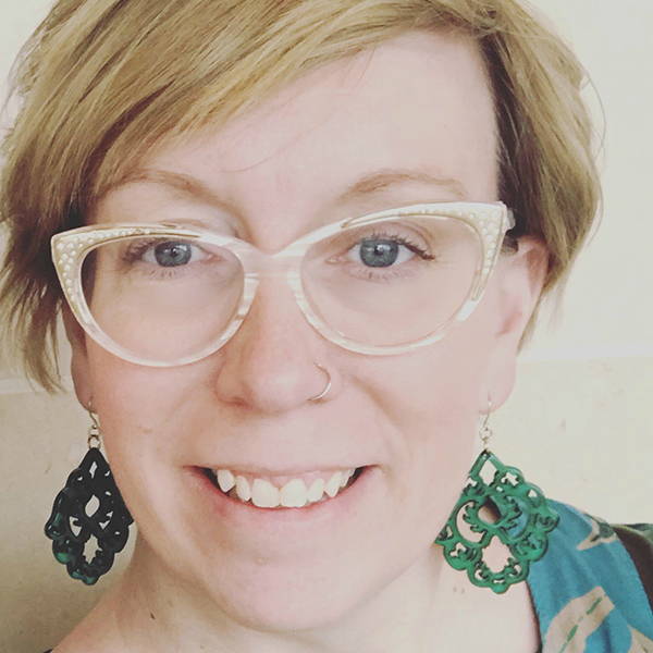 A woman wearing glasses and green earrings.