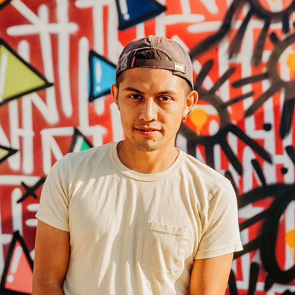 A young man standing in front of a colorful graffiti wall.