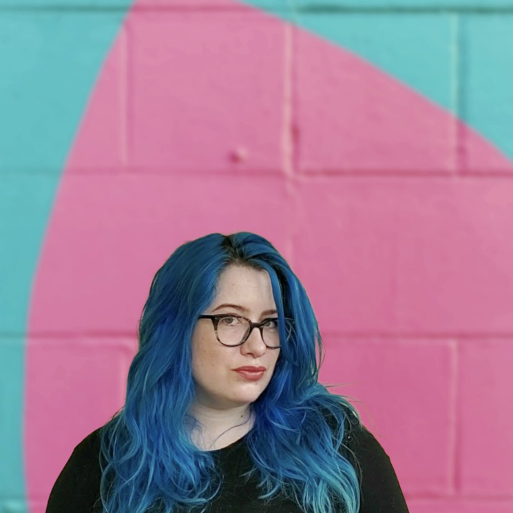 A woman with blue hair standing in front of a pink and blue wall.