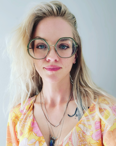 A blonde woman wearing glasses and a floral top.