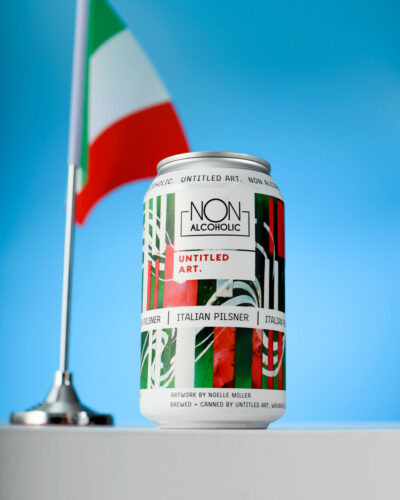 An italian flag sits on a table next to a can of beer.