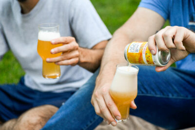 Two men drinking beer in a grassy area.