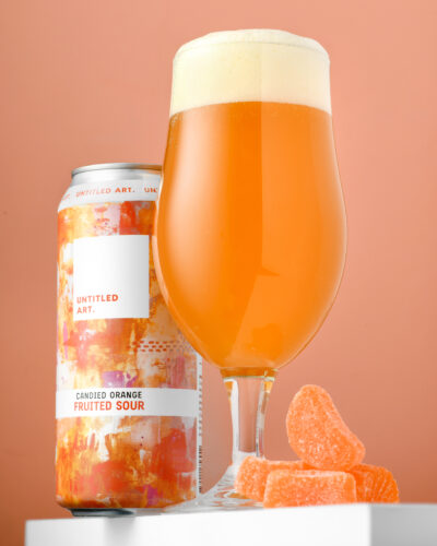 A glass of orange beer next to a can of gummy bears.