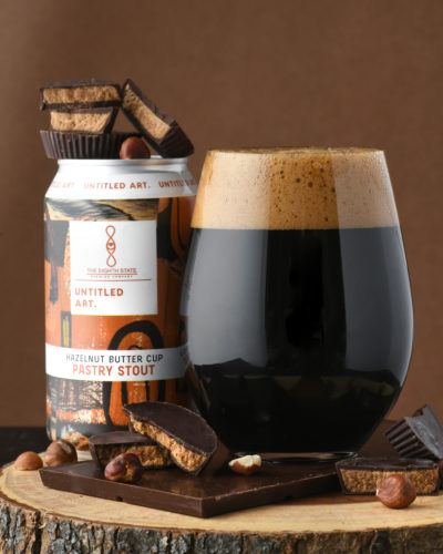A glass of dark beer next to a can of chocolate and nuts.