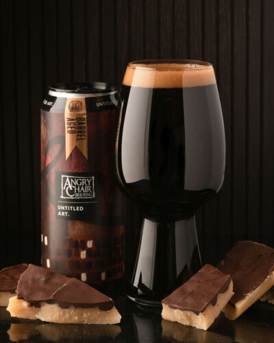 A glass of dark beer next to a can of chocolate.