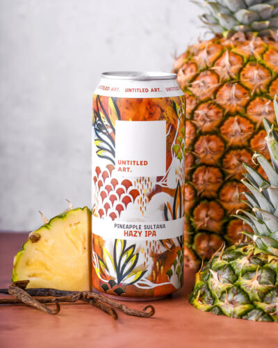 A can of pineapple beer next to a pineapple.