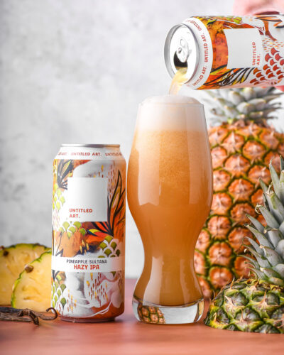 A beer is being poured into a can next to pineapples.