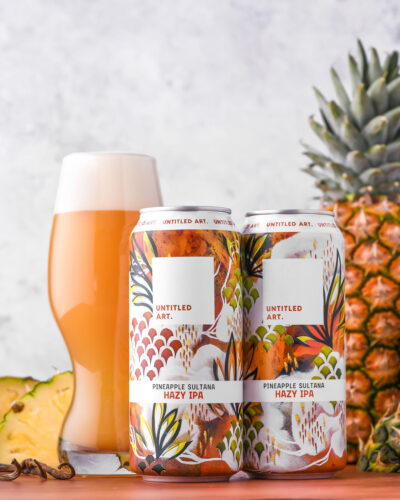 Two cans of pineapple beer with a glass next to them.