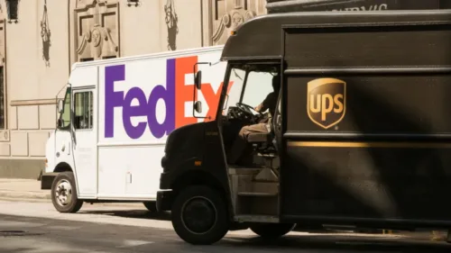 Two UPS/FedEx Ground Shipping trucks parked on a street.
