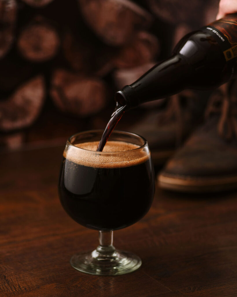 A person pouring a dark beer into a glass.