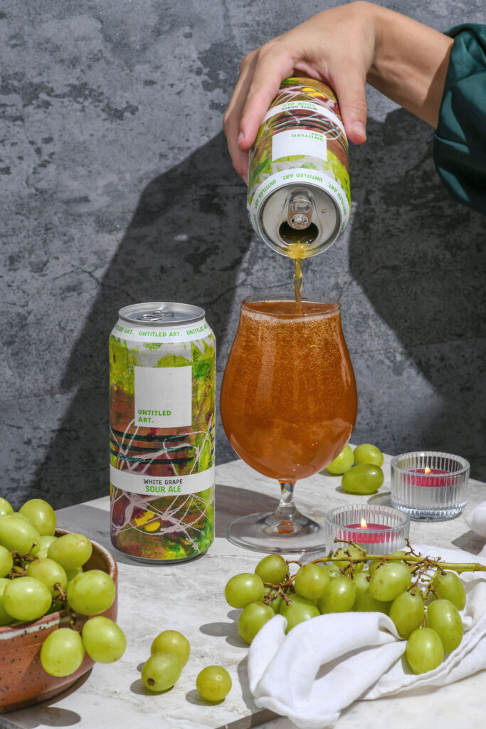 A woman pouring a can of beer into a glass of grapes.