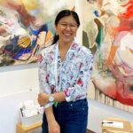 A smiling woman standing in front of a painting.
