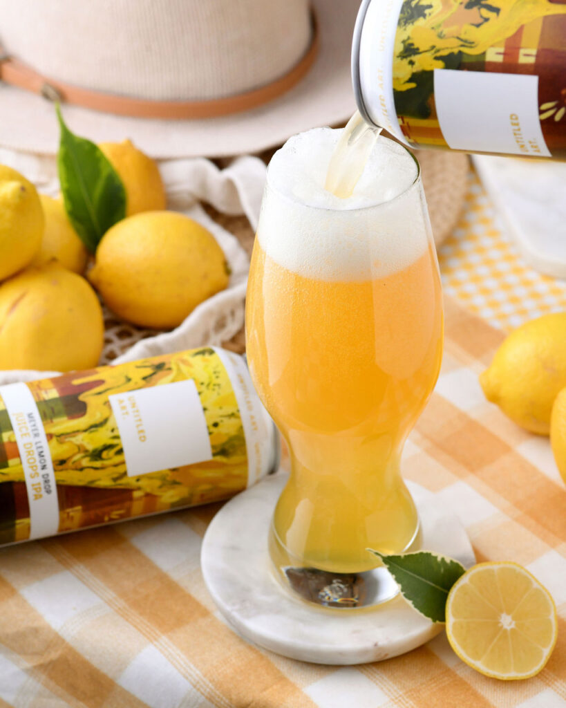 Pouring a refreshing citrus beer into a glass with fresh lemons in the background.